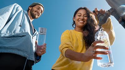 Frau füllt draußen an einem öffentlichen Wasserhahn eine BRITA Trinkflasche mit Filter